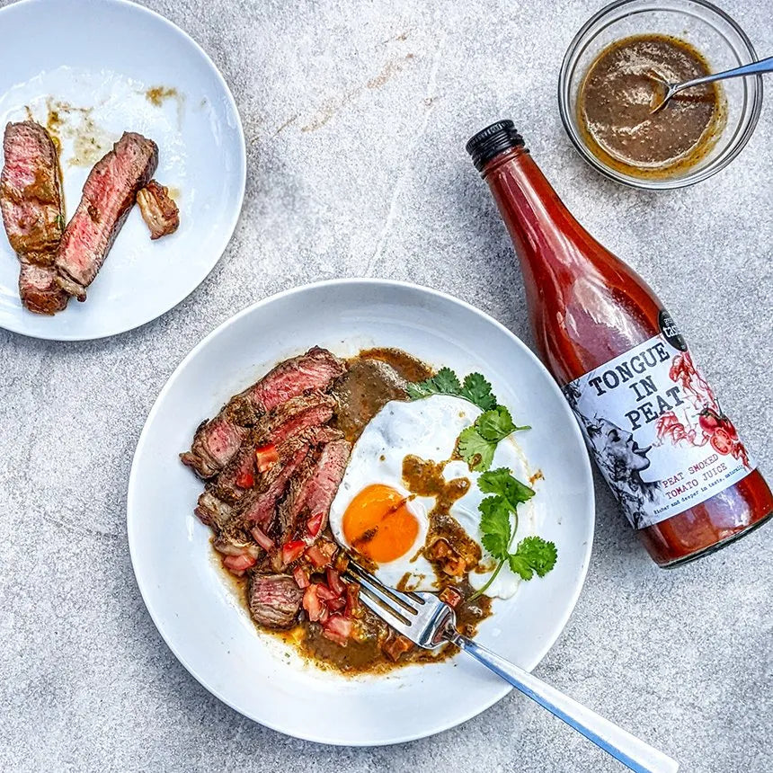 bottle of tongue in peat smoked tomato juice next to plates of steak and eggs