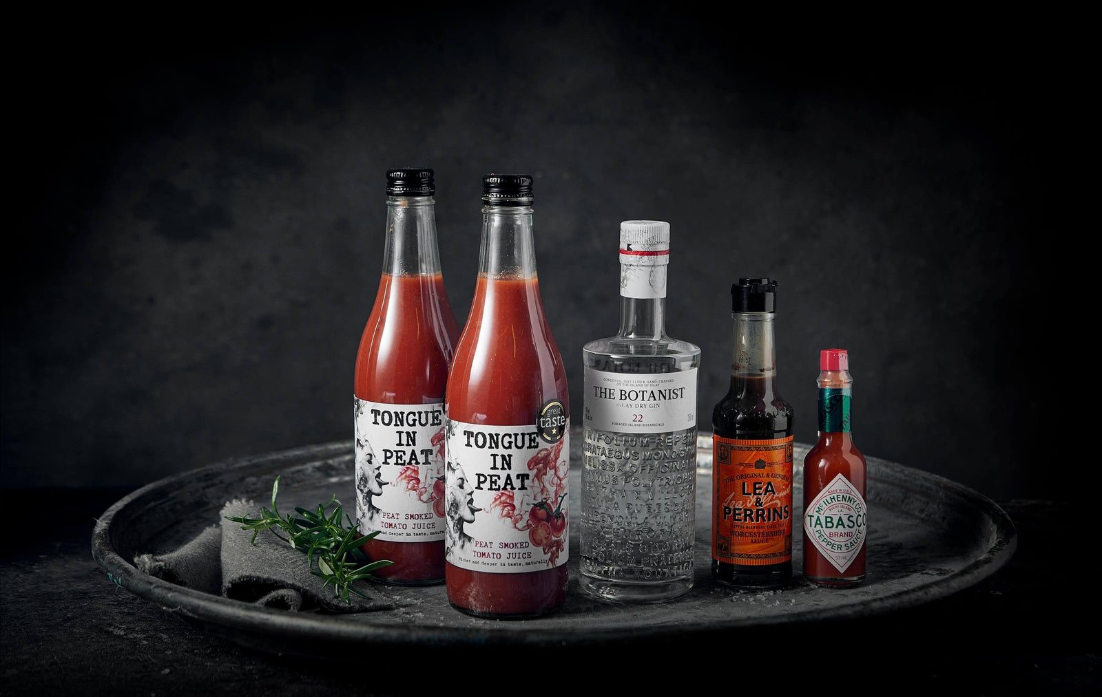 a plate with two bottles of tongue in peat smoked tomato juice, a bottle of Botanist vodka, tabasco and worcester sauce