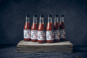 6 bottles of Tongue in Peat smoked tomato juice standing on a wooden board