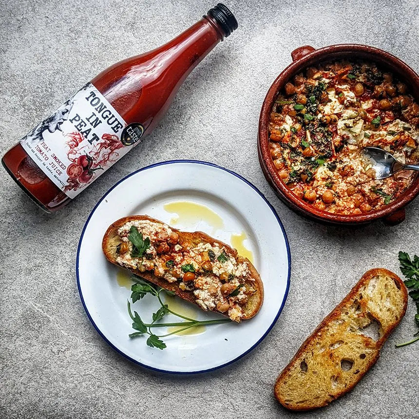 bottle of tongue in peat smoked tomato juice next to baked bread with feta and bowl of chickpeas, harissa and parsley