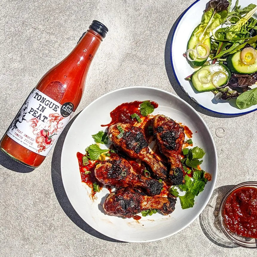 bottle of tongue in peat smoked tomato juice next to plates of BBQ chicken, salad, and chilli sauce