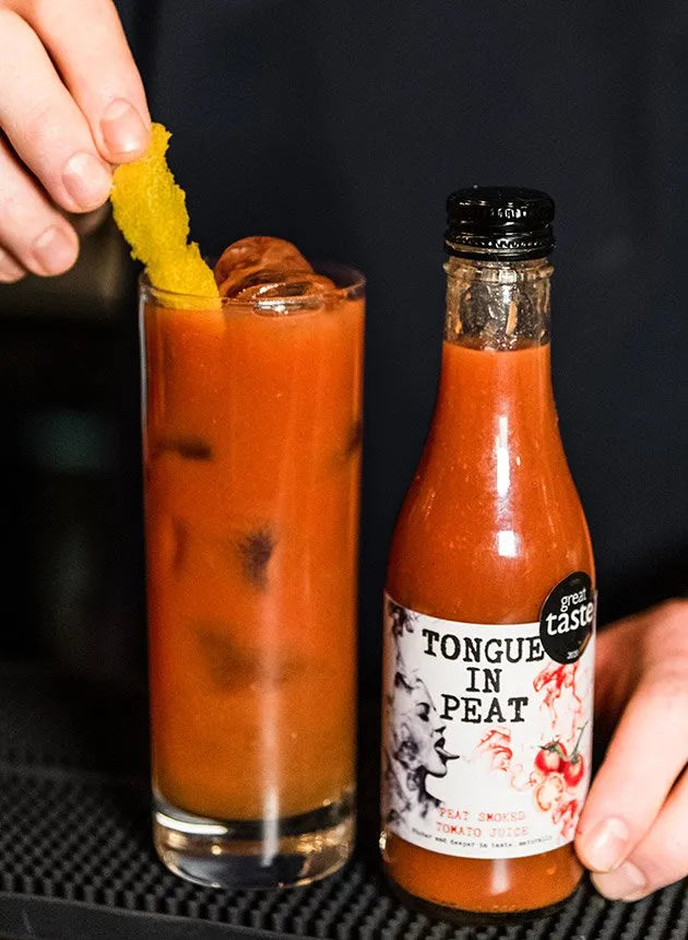 bottle of tongue in peat smoked tomato juice next to a glass of bloody joseph cocktail