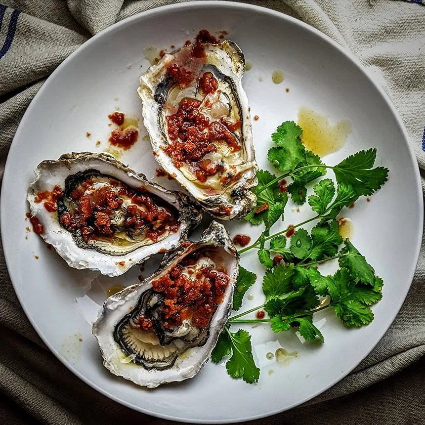 three oysters on a plate with parsley and bloody mary-style sauce made with peat smoked tomato juice