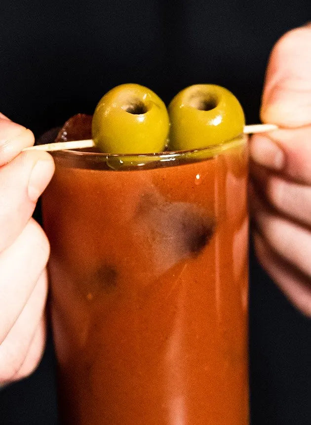close up of a red snapper cocktail, garnished with two green olives on a toothpick